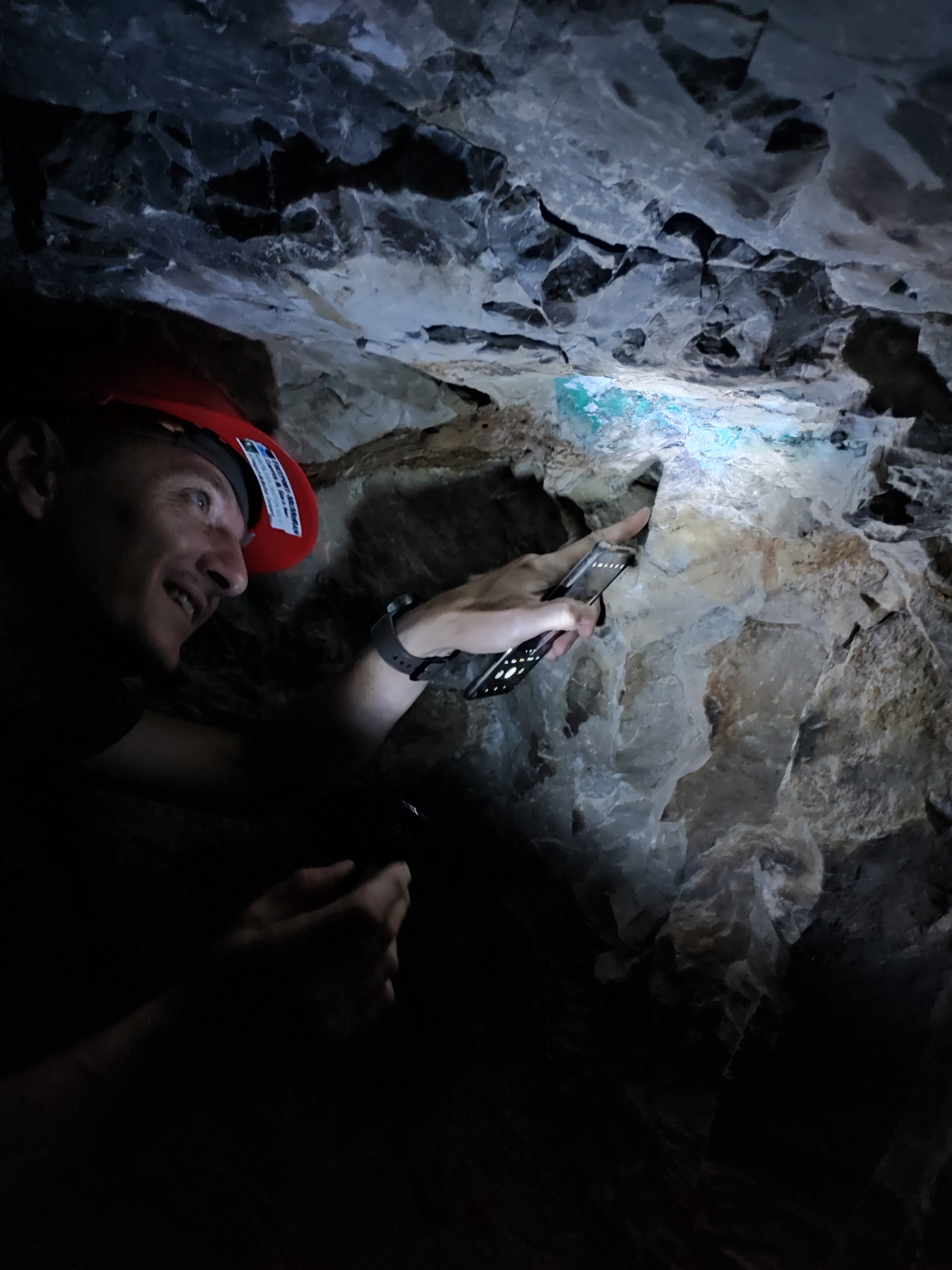 Geologist examining turquoise malachite mineralisation on a tunnel wall by torchlight