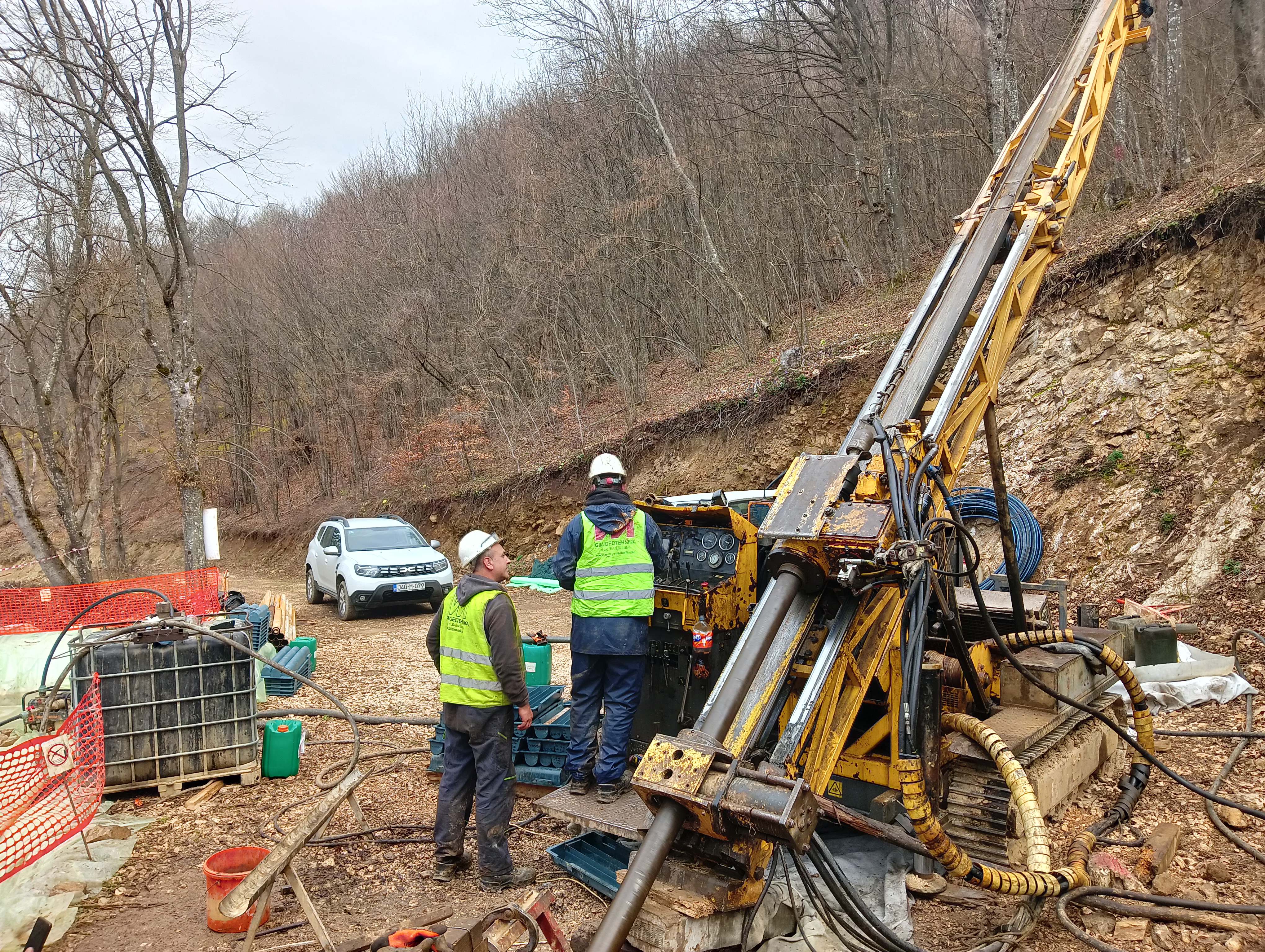 Field crew in hi-vis and hard hats operating a diamond drill rig at a forested drill site